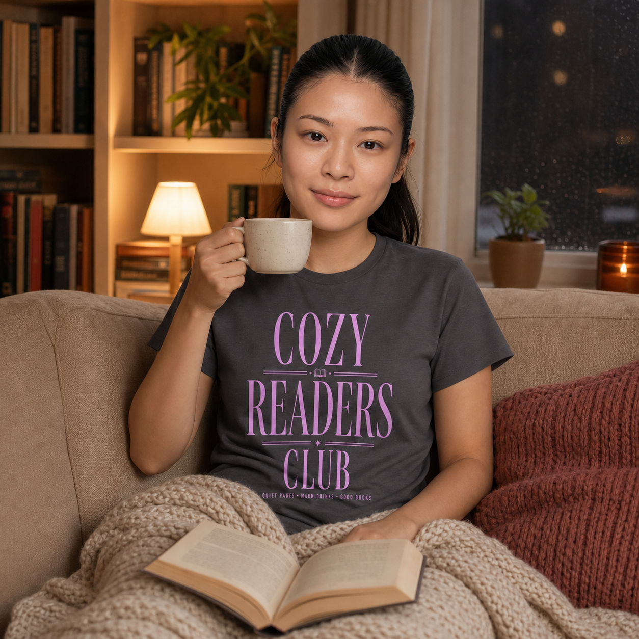 Woman reading in a cozy evening setting while wearing the Charcoal Cozy Readers Club tee