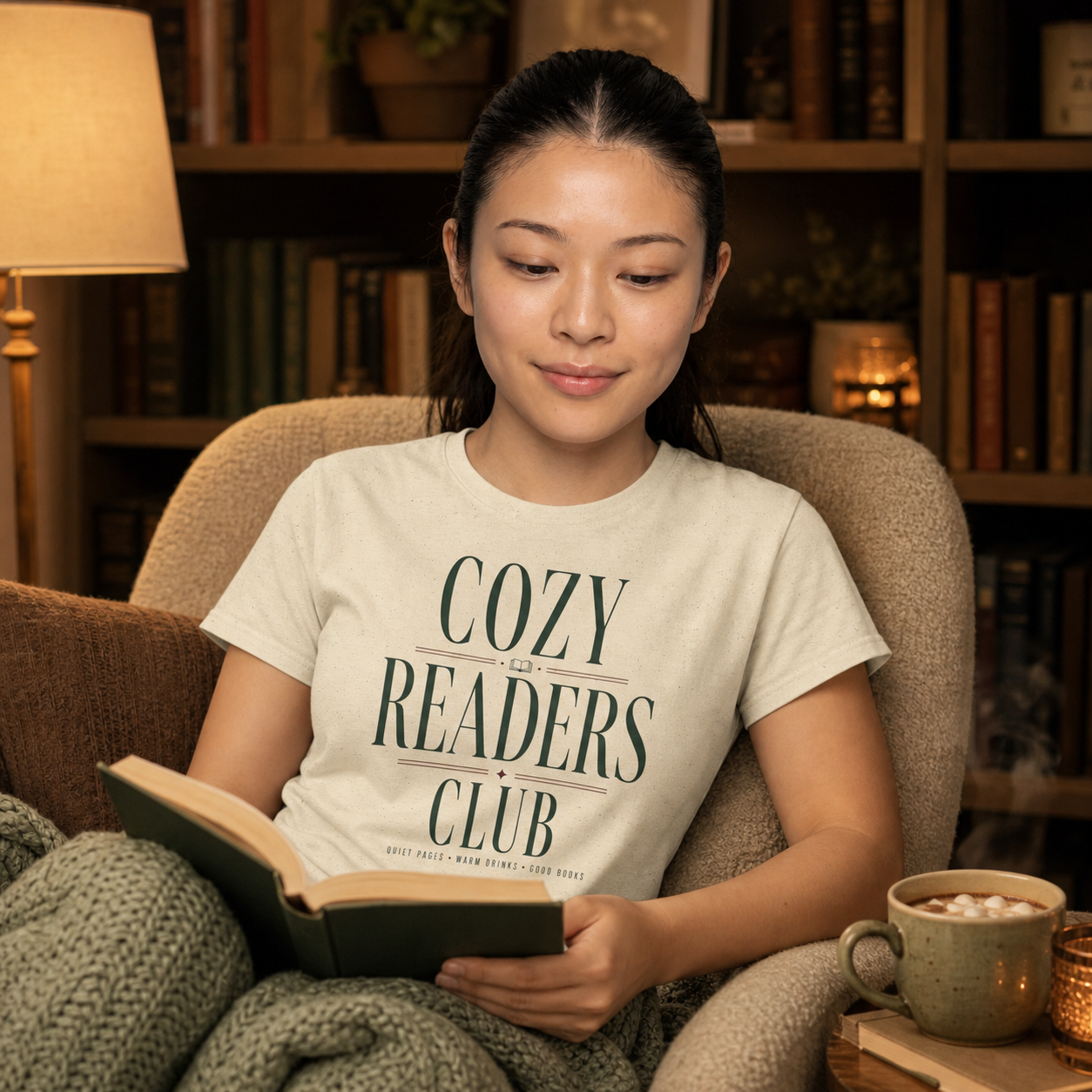 Woman reading in a cozy armchair while wearing the Natural Cozy Readers Club tee